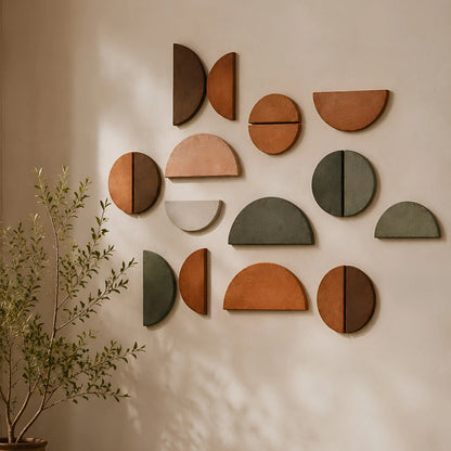 A set of terracotta and earthy brown semi-circular wall art pieces arranged in a decorative cluster on a beige wall, with soft sunlight casting shadows and a potted plant visible in the lower left corner.