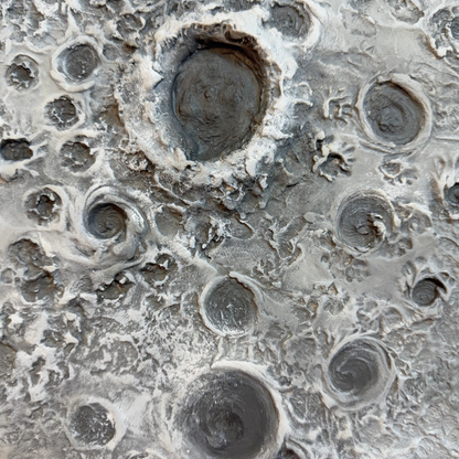 A close-up abstract texture or print featuring a mottled gray and off-white surface with multiple circular and crater-like forms.